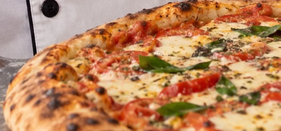 Pizza recém-saída do forno, com borda tostada, tomate e manjericão